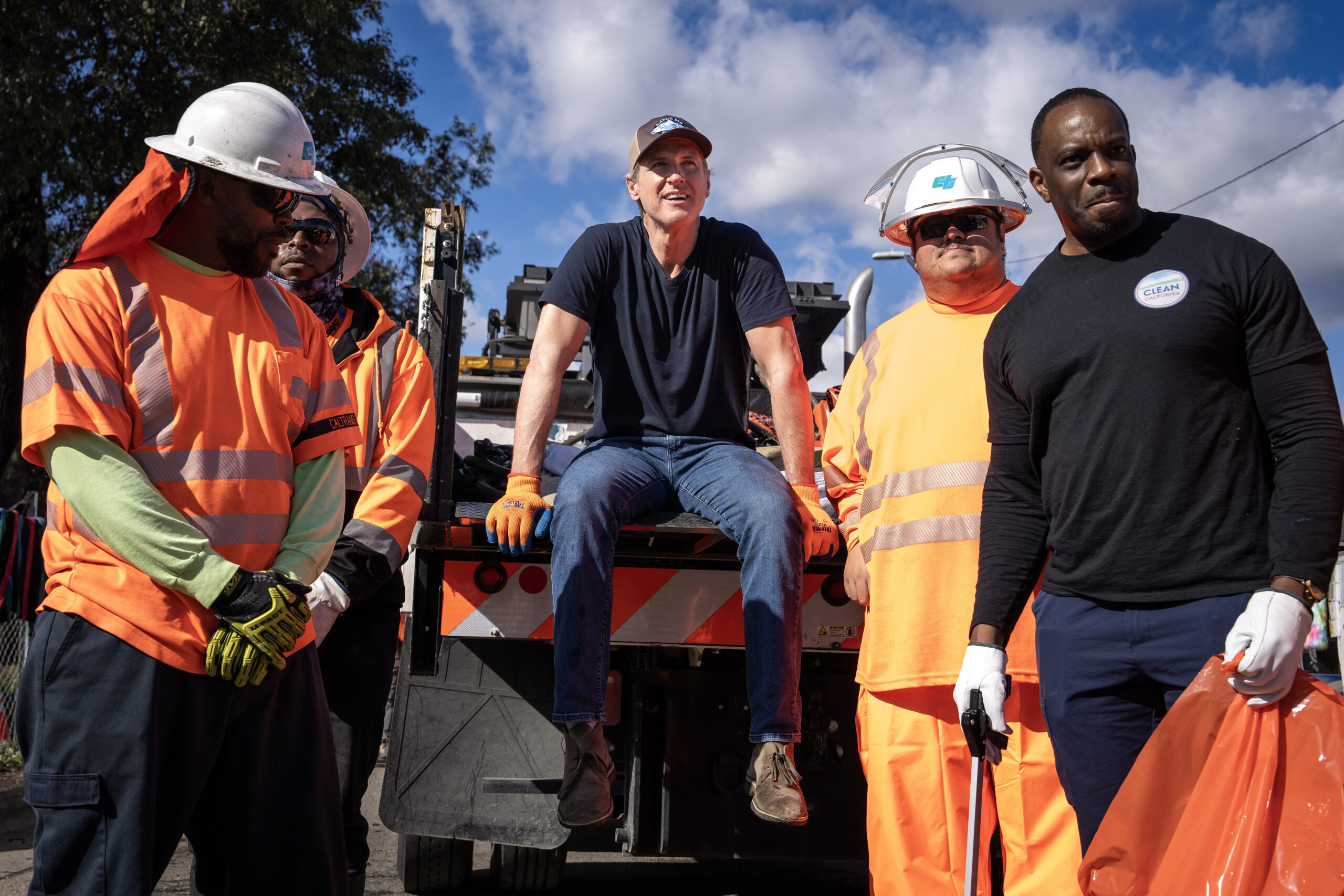 Governor Newsom sitting on the back of a utility truck surrounded by CalTrans workers.